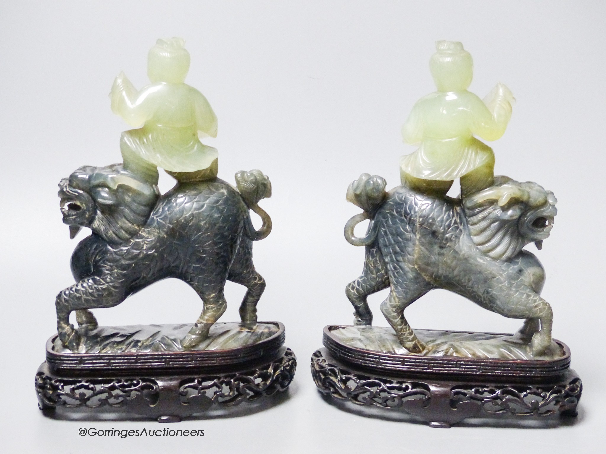 A pair of Chinese bowenite Jade figures of boys riding a qilin, mid 20th century, wood stands